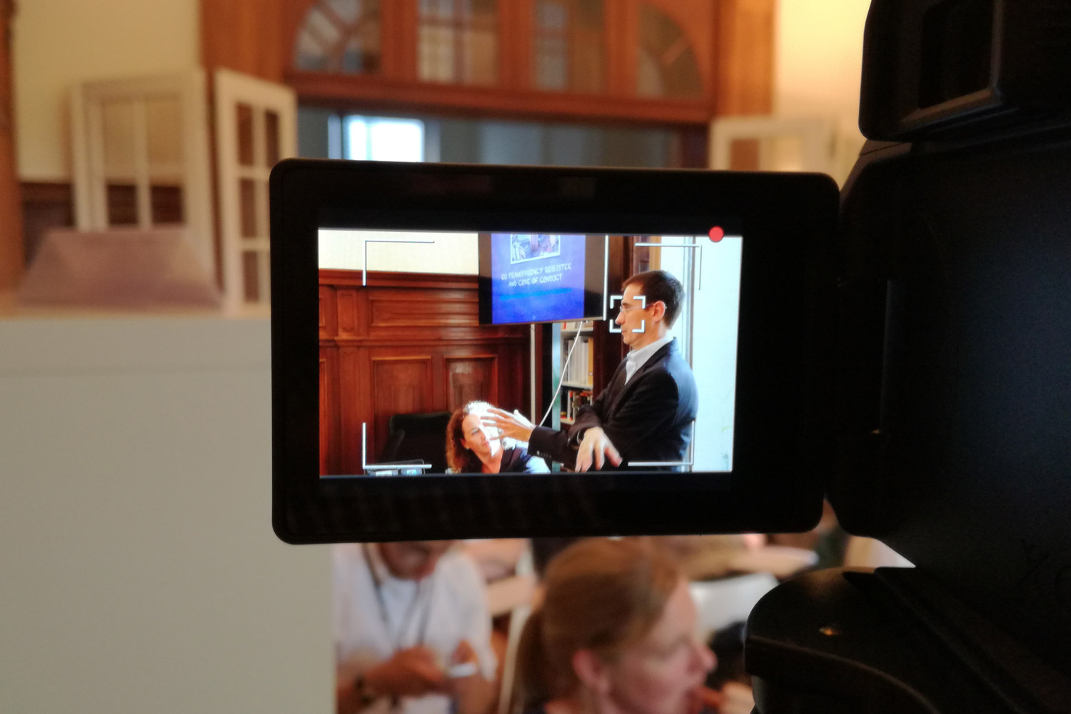 A man is seen on a camera screen giving a presentation
