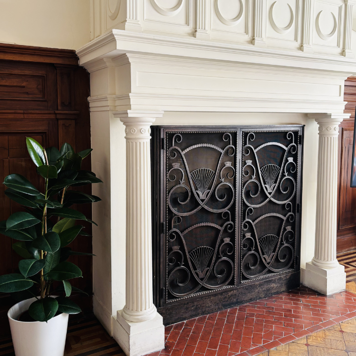 Ornate white marble fireplace with decorative ironwork screen and potted plant in the training venue